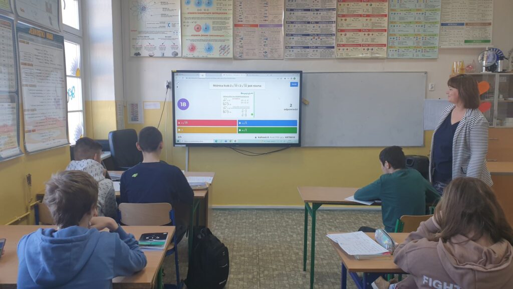 Na zdjęciu widoczni uczniowie i monitor interaktywny z aplikacją kahoot, uczniowie rozwiązują quiz podsumowujący lekcję. 