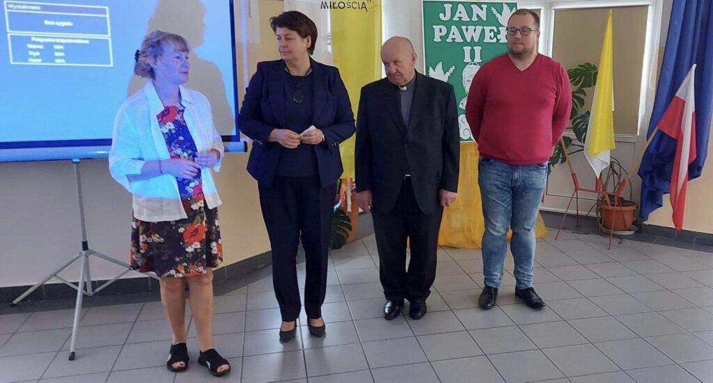 Na tle ekranu z prezentacja stoją cztery osoby, dwie kobiety i dwóch mężczyzn.
