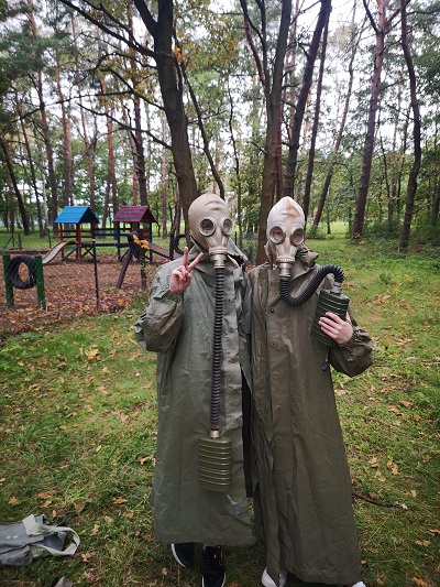 na tle drzew w parku dwie dziewczynki pozują w płaszczach i maskach przeciwgazowych