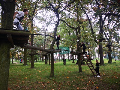 cztery dziewczynki zapięte w uprzęże pokonują tor przeszkód w parku linowym na wysokości kilku metrów