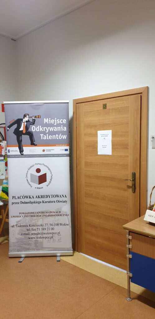 Na zdjęciu widoczne z prawej strony drzwi z umieszczoną na nich kartką z napisem „Dolnośląskie Konkursy zDolny Ślązak, rok szkolny 2022/2023”, z lewej strony banner z napisem „Miejsce odkrywania talentów” i danymi teleadresowymi PCEiPPP w 