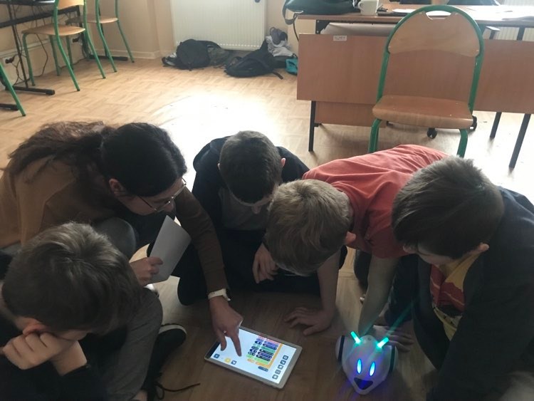Na zdjęciu widoczni uczniowie i prowadząca. Nachylają się tabletem i układają program do gry.