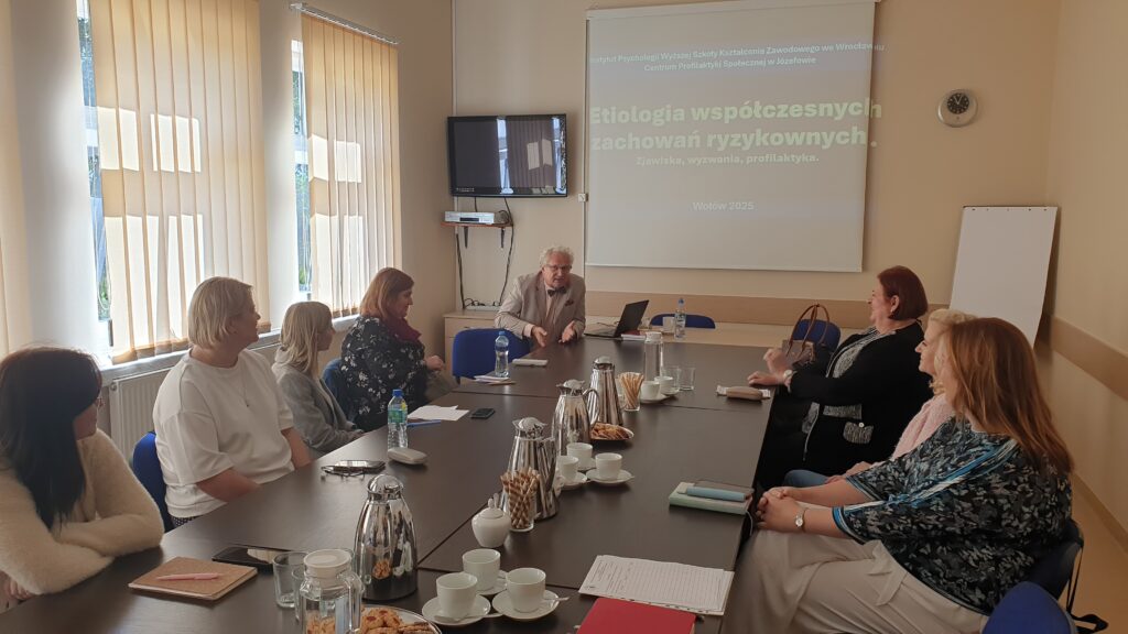 przy stole siedzi grupa osób w tle wyświetlany slajd prezentacji