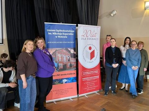 Aula szkolna, na środku kobiety, które mówią coś do uczestników.