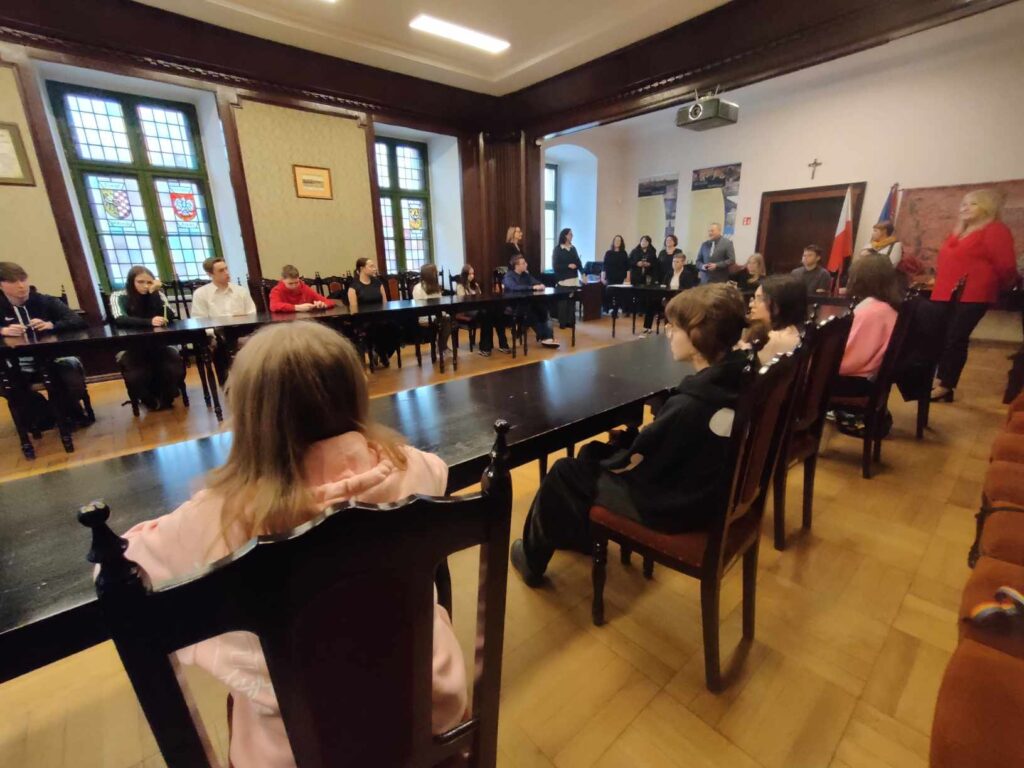 2. Zdjęcie przedstawia grupę uczniów, którzy siedzą przy stołach w sali konferencyjnej Starostwa Powiatowego w Wołowie.