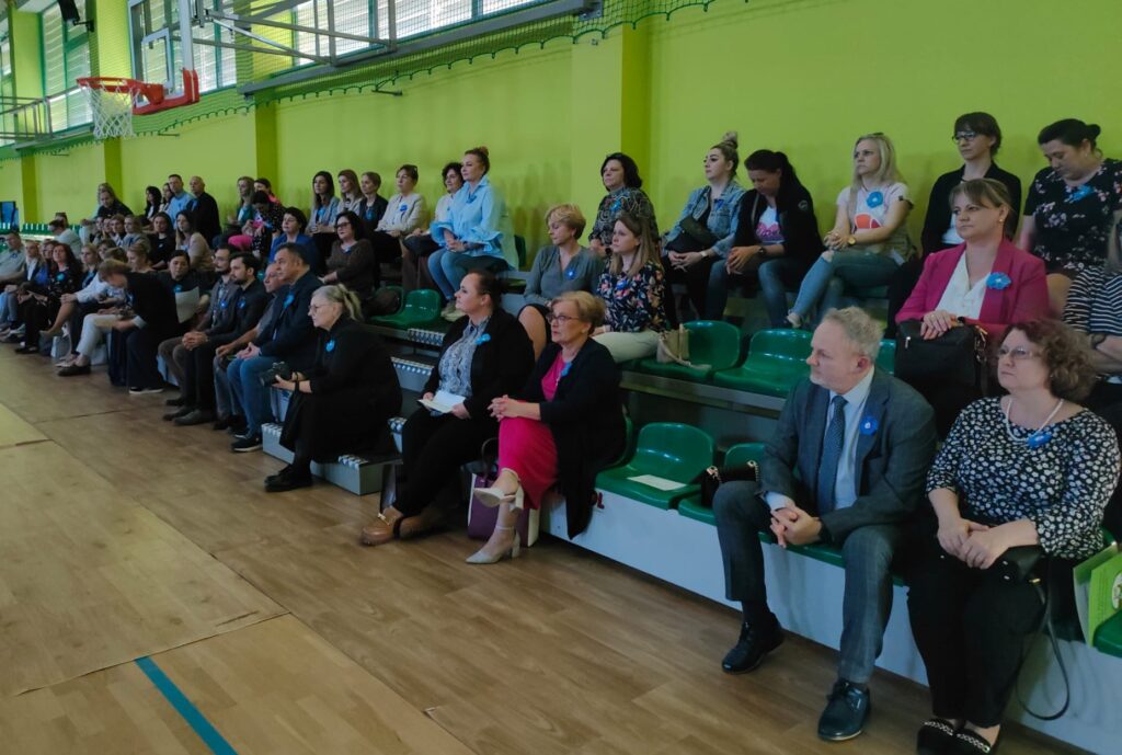 Na widowni w sali gimnastycznej siedzą uczestnicy konferencji.