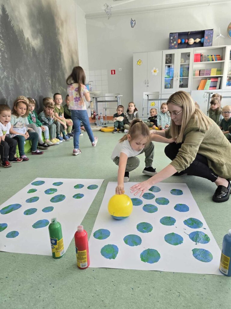 Sala lekcyjna, na pierwszym planie nauczycielka z uczennica. Na białej kartce odbijają zielona plamę.