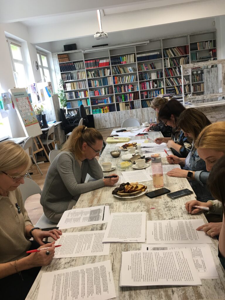 Sala biblioteczna, na środku stoły. Przy stolikach siedzą kobiety. Coś piszą.