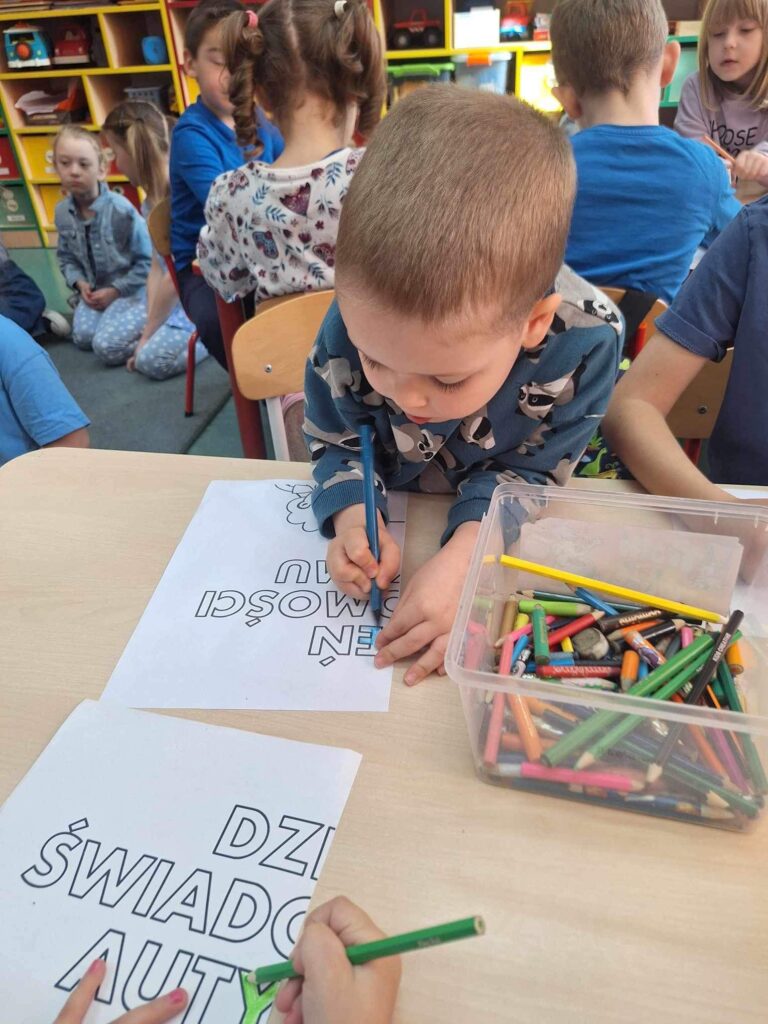 Przy stoliku siedzą dzieci i malują na niebiesko fragment plakatu.