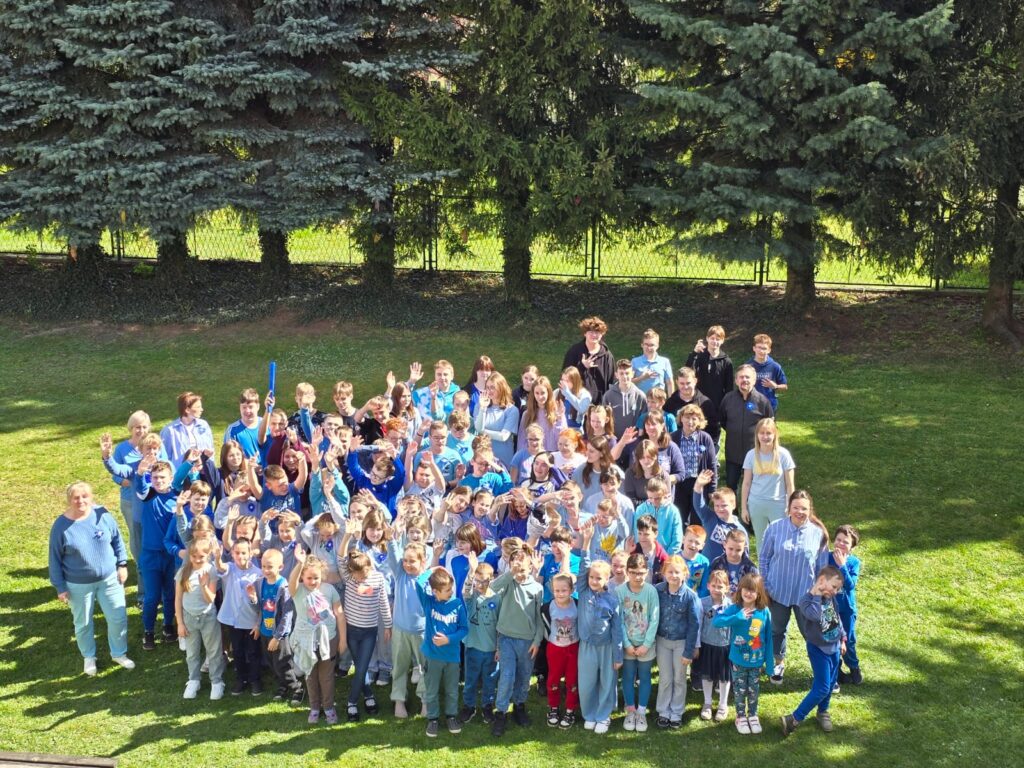 Grupa dzieci dorosłych na podwórku szkolnym. Wszyscy ubrani na niebiesko.

