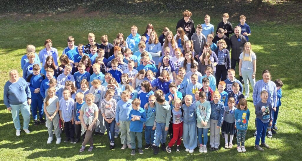 Grupa dzieci dorosłych na podwórku szkolnym. Wszyscy ubrani na niebiesko.