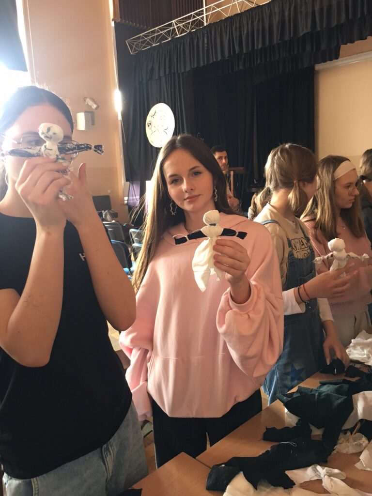 Aula szkolna, przy stoliku stoją dwie dziewczynki ze wykonanymi lalkami.