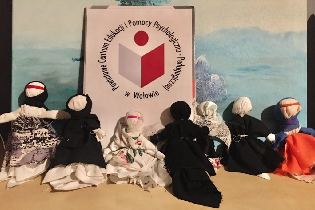 Plansza z logiem firmy- organizatora spotkania. Na dole siedzą wykonane podczas warsztatów laleczki.