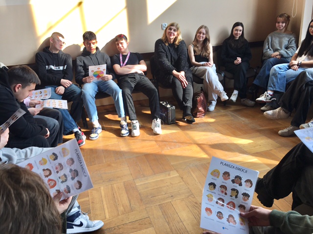 Aula szkolna, na środku uczniowie z nauczycielami.