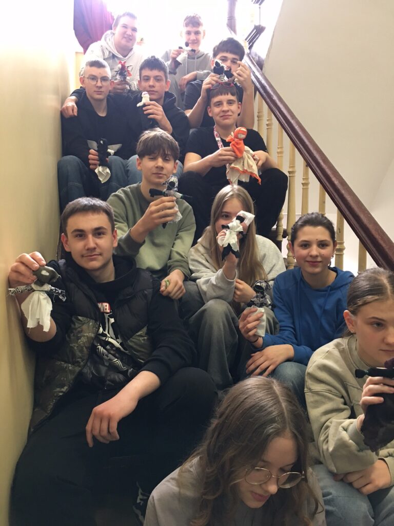 Korytarz szkolny, na schodach uczniowie zwykonanymi przez siebie Żądanicami. 