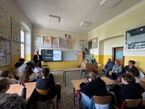 Sala klasowa wypełniona uczniami słuchającymi prelegentki, stojącej przed zieloną tablicą szkolną.