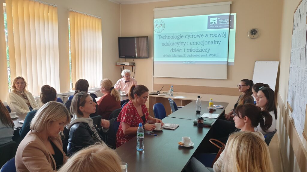 przy stole siedzi grupa osób w tle wyświetlany slajd prezentacji