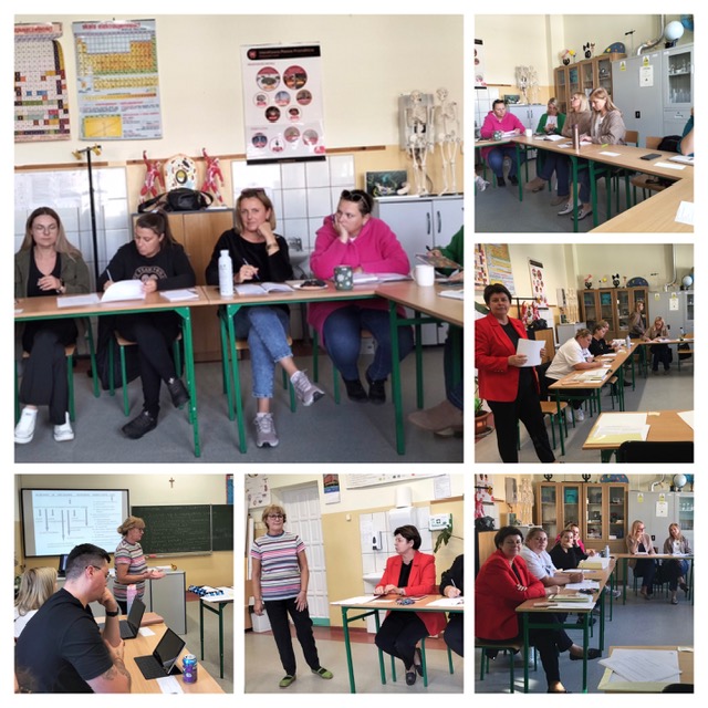 Klasa, w której przy stolikach siedzą nauczyciele. Na stolikach leżą kartki, notatniki. Kobieta prowadzi spotkanie. Dwie kobiety stoją przed siedzącymi przy stolikach osobami.