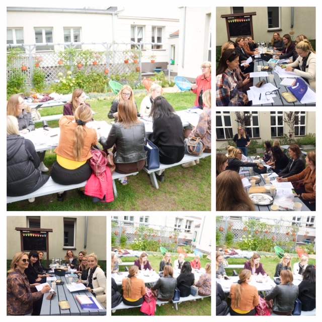 Zielona klasa na świeżym powietrzu, na środku stoły. Wokół siedzą nauczyciele. Na stole stoją talerzyki z ciastem i kubki i termosy. Kobieta stoi z przodu i coś mówi.