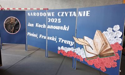 NA ŚRODKU STOI NIEBIESKI BANER Z NAPISEM NARODOWE CZYTANIE 2025 JAN KOCHANOWSKI PIEŚNI , FRASZKI, TRENY