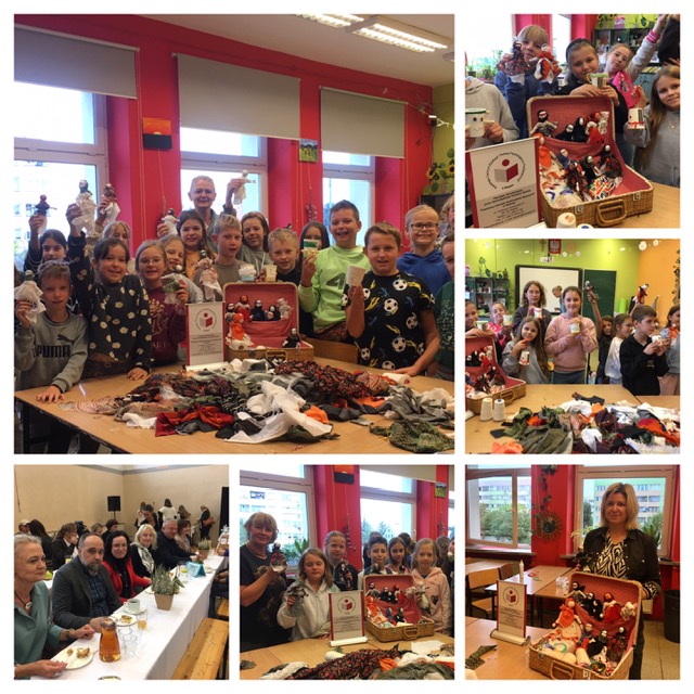 Sala lekcyjna. Przy stole z materiałami stoją dzieci i dorośli. W ręku trzymają kolorowe lalki kubki. Przy stole siedzą dorośli, mężczyźni i kobiety.
: