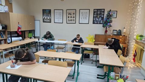 Sala lekcyjna, w ławkach siedzą uczniowie i piszą. 