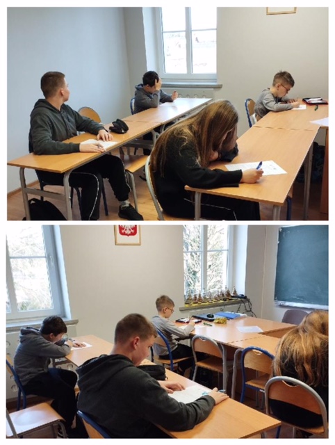 Sala lekcyjna, przy stolikach siedzą uczniowie i piszą. 