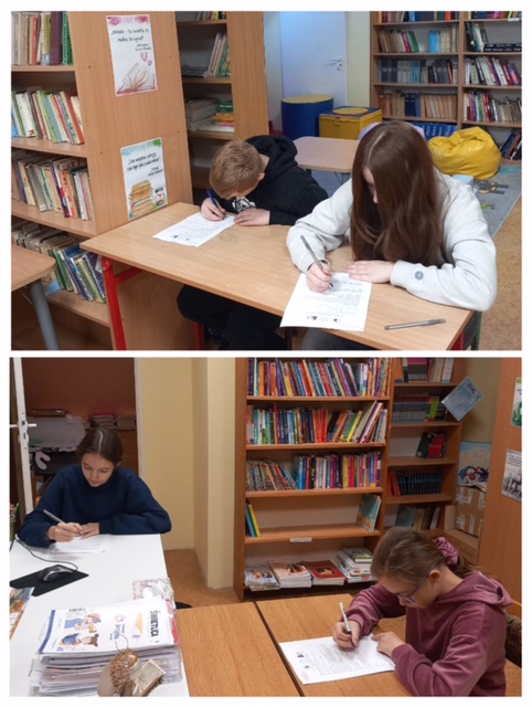 Biblioteka szkolna. Czworo dzieci siedzi przy stolikach i cos pisze. W tle regały z książkami.