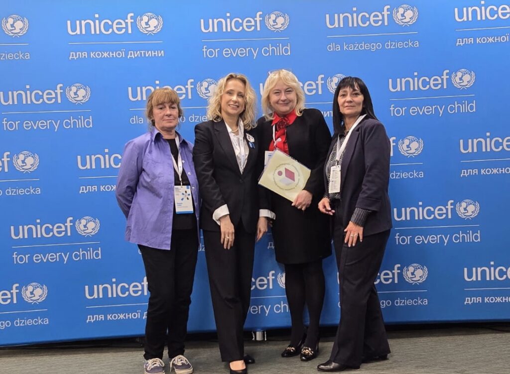 Na tle niebieskiej planszy projektu, z białymi napisami Unicef, stoją cztery kobiety