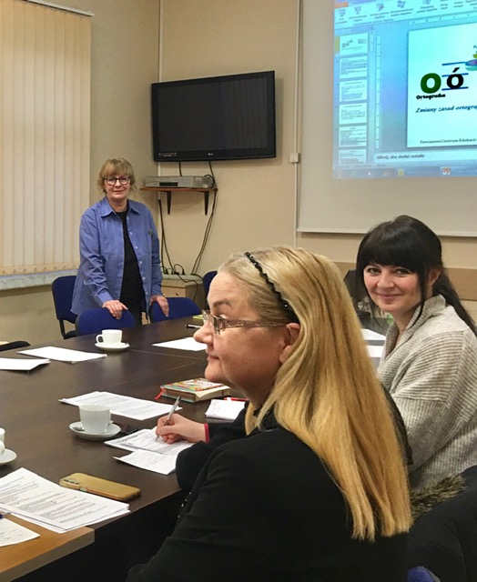 Sala konferencyjna. Przy wspólnym stole siedzą kobiety. Mają na pulpicie kartki. Przed nimi kobieta prowadząca spotkanie.