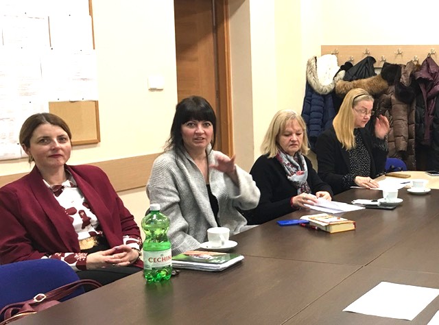 Sala konferencyjna. Przy wspólnym stole siedzą kobiety. Mają na pulpicie kartki. 