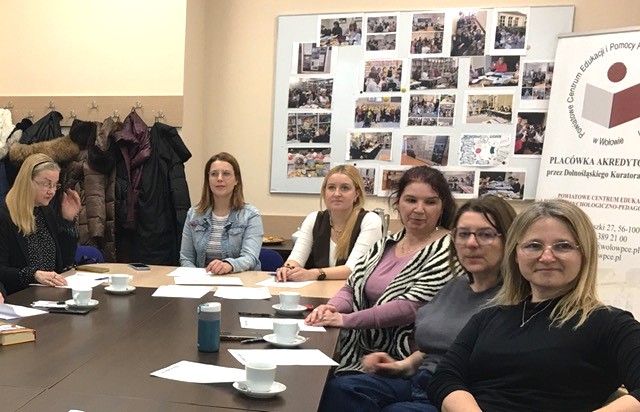 Sala konferencyjna. Przy wspólnym stole siedzą kobiety. Mają na pulpicie kartki. 