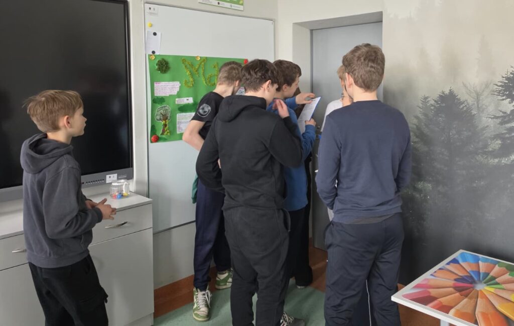 Sala lekcyjna, przy drzwiach uczniowie.