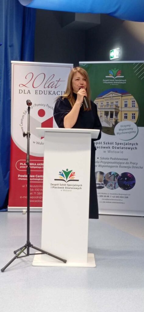 na zdjęciu dwa banery za nimi stoi kobieta przy mównicy 
