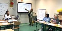 Sala lekcyjna, siedzą osoby a przed ekranem prowadząca spotkanie.